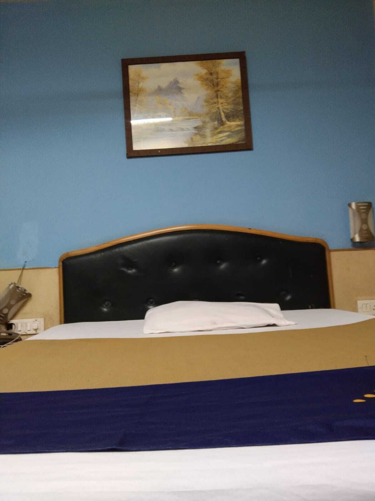 A bed with a dark headboard, a white pillow, and a blue bedspread in a room with blue walls and a framed picture on the wall.