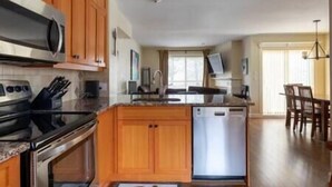 A kitchen with wooden cabinets, a stainless steel oven, a dishwasher, and a dining area with a table and chairs.