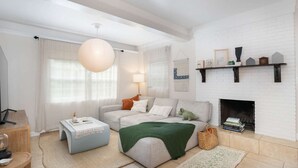 A living room with a white brick fireplace, a sofa, a coffee table, and a hanging light fixture. - Thai · Cozy Ginger Home with Pool · 12 minutes to Beach · Pet-Friendly (Melbourne)