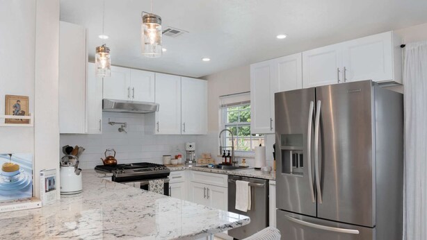 A modern kitchen with white cabinets, a stainless steel refrigerator, a gas stove, and pendant lighting. - Thai · Cozy Ginger Home with Pool · 12 minutes to Beach · Pet-Friendly (Melbourne)
