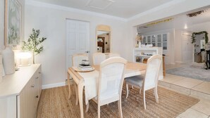 A dining area with a wooden table, white wicker chairs, and a woven rug. - Thai · Cozy Ginger Home with Pool · 12 minutes to Beach · Pet-Friendly (Melbourne)