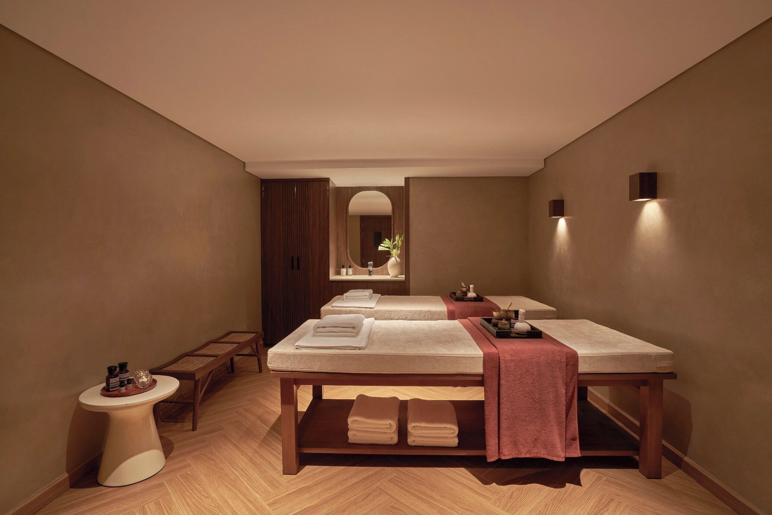 A spa room with two massage tables, a small side table, and a mirror.