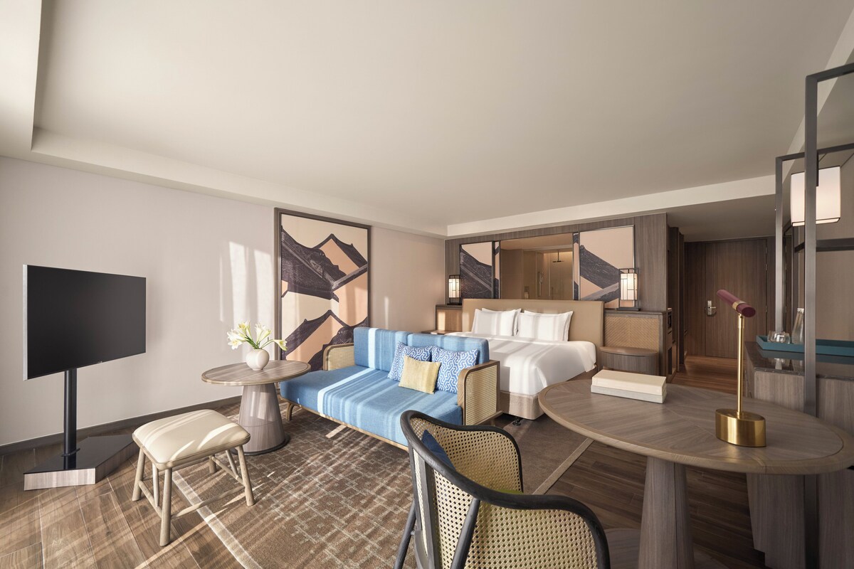 A modern hotel room with a sofa, a bed, a dining table, and a TV.
