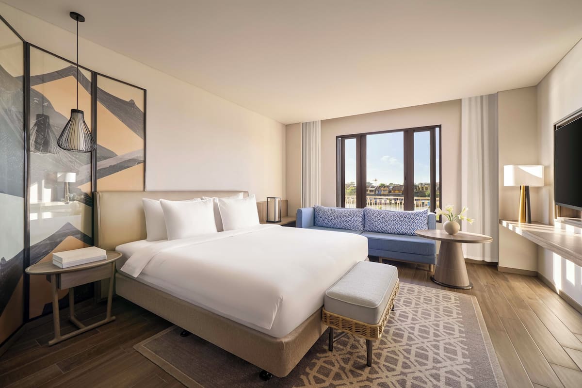 Habitación de hotel con una cama grande, un sofá, un televisor, un cuadro y vistas a la ciudad.