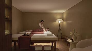 A massage room with a massage table, towels, a massage chair, a lamp, and a small table with a vase of flowers.