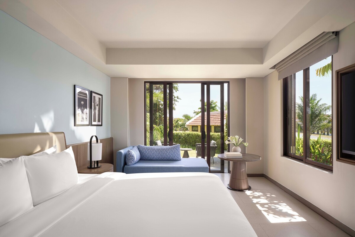 Una camera d'albergo moderna con un letto grande, un divano, un tavolino e vista sull'esterno.