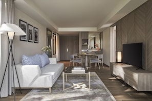 A modern living room with a sofa, coffee table, and TV. There is a dining area with chairs and a table.
