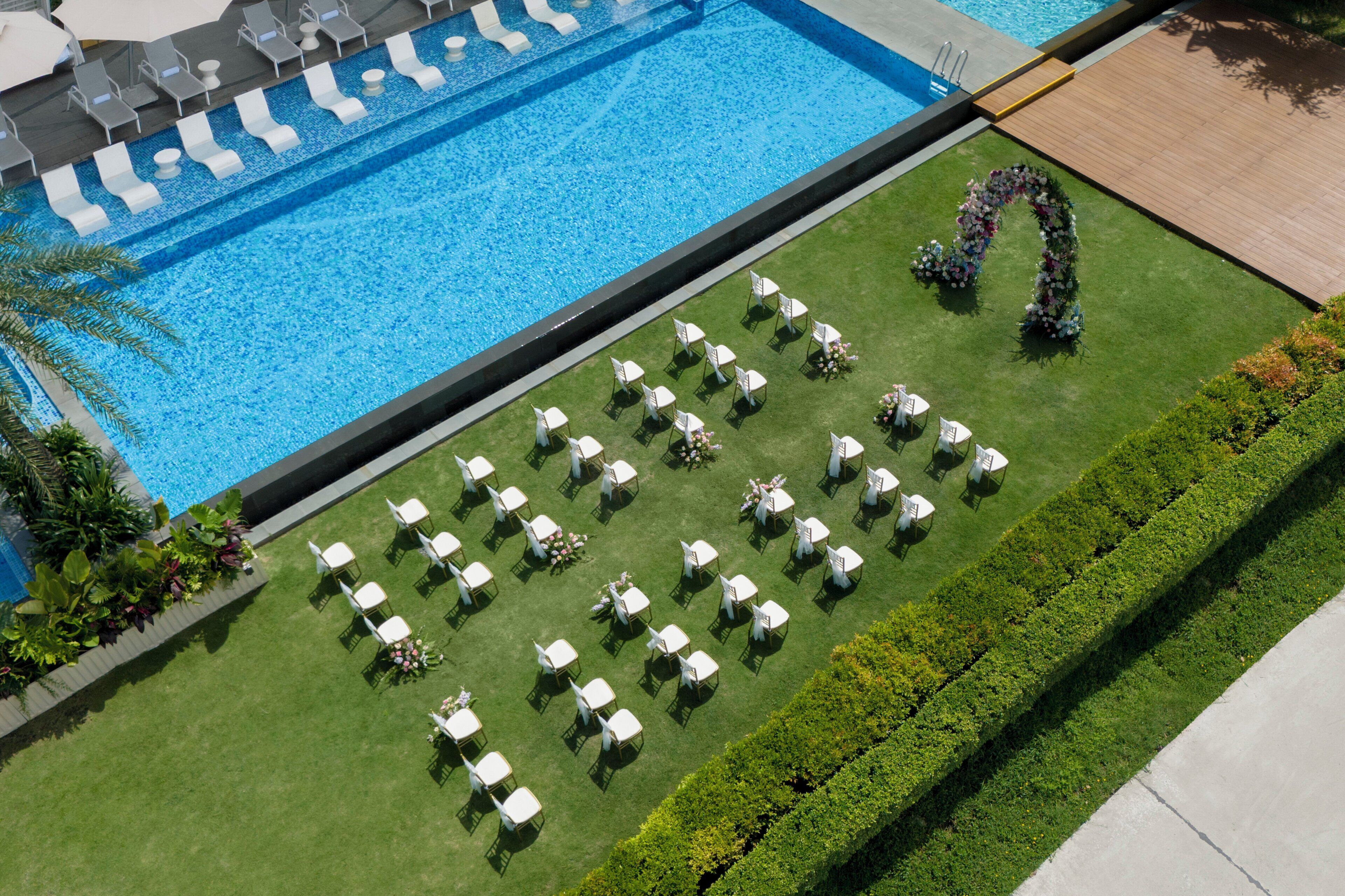 An aerial view of a pool area with lounge chairs and tables arranged for an event.