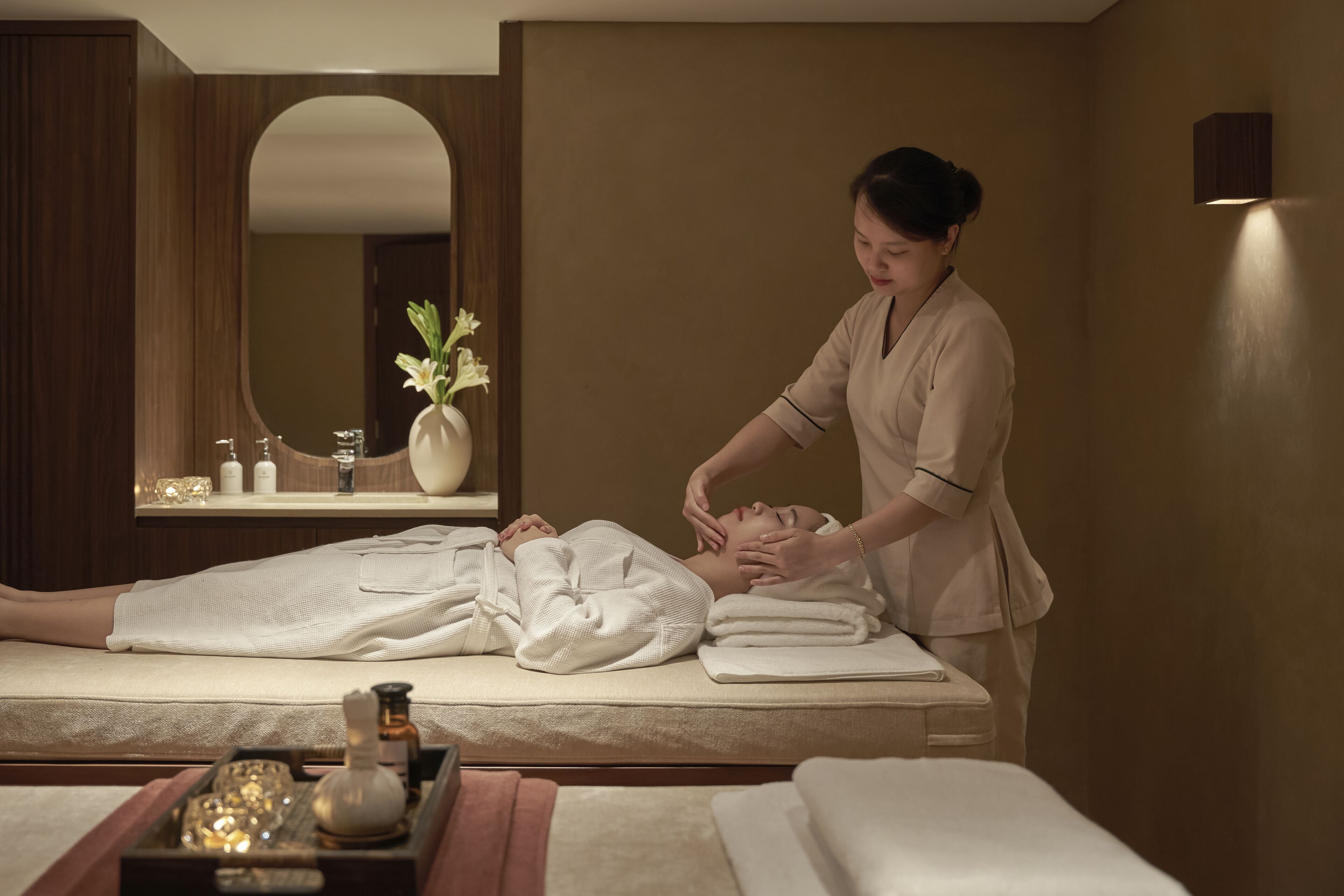 A spa room with a massage table, a mirror, and a vase with flowers.