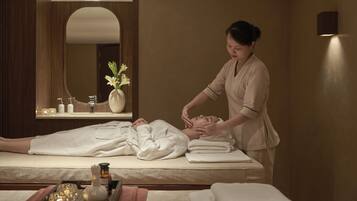 A spa room with a massage table, a mirror, and a vase with flowers.