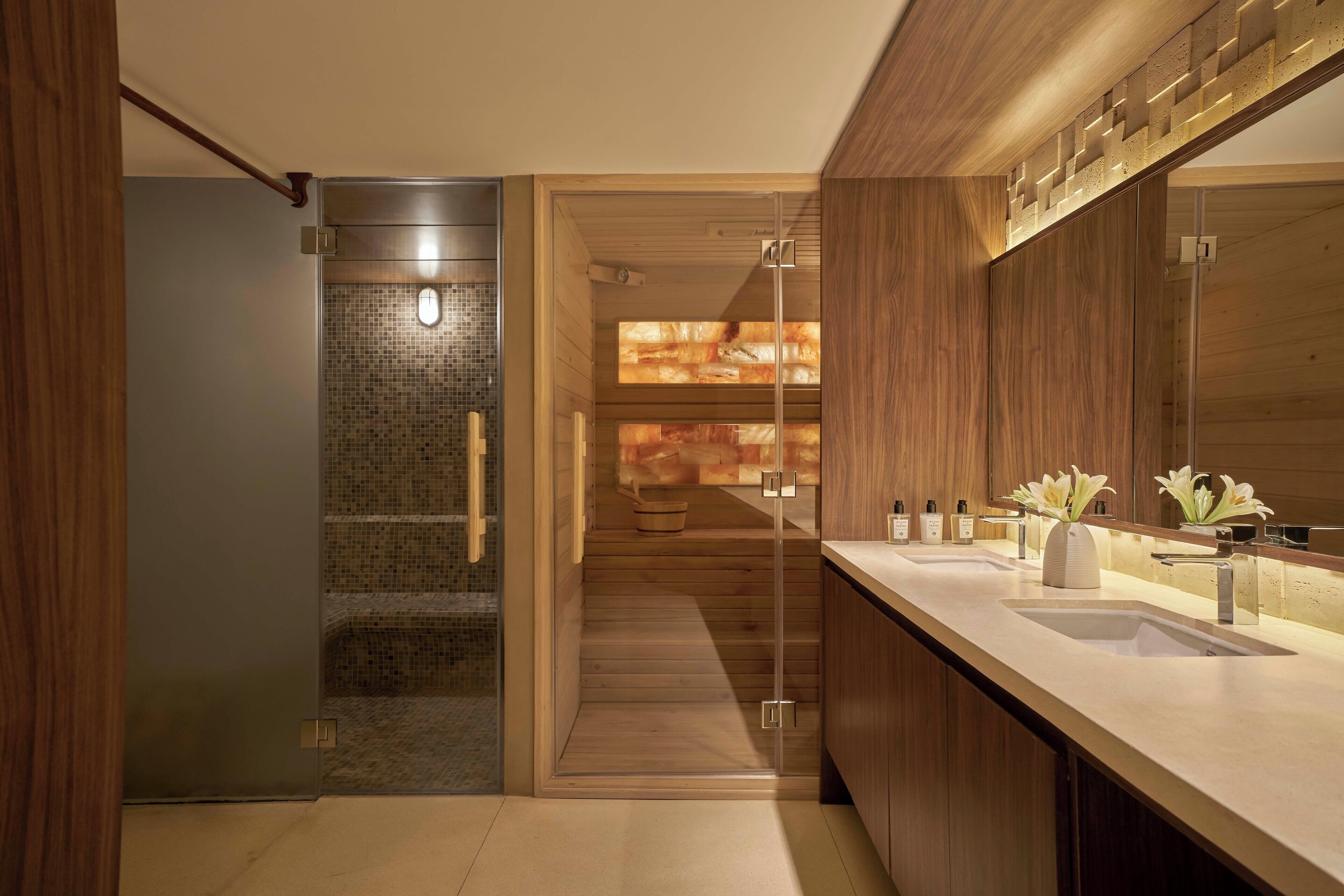 A modern bathroom with a glass shower enclosure, wooden flooring, and a large mirror.