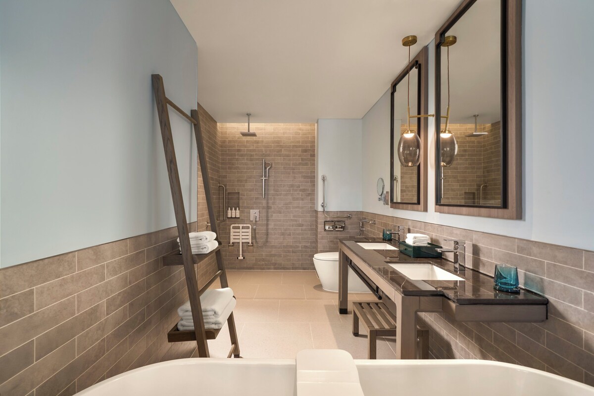 A modern bathroom with a bathtub, two sinks, a shower, and a wooden ladder.