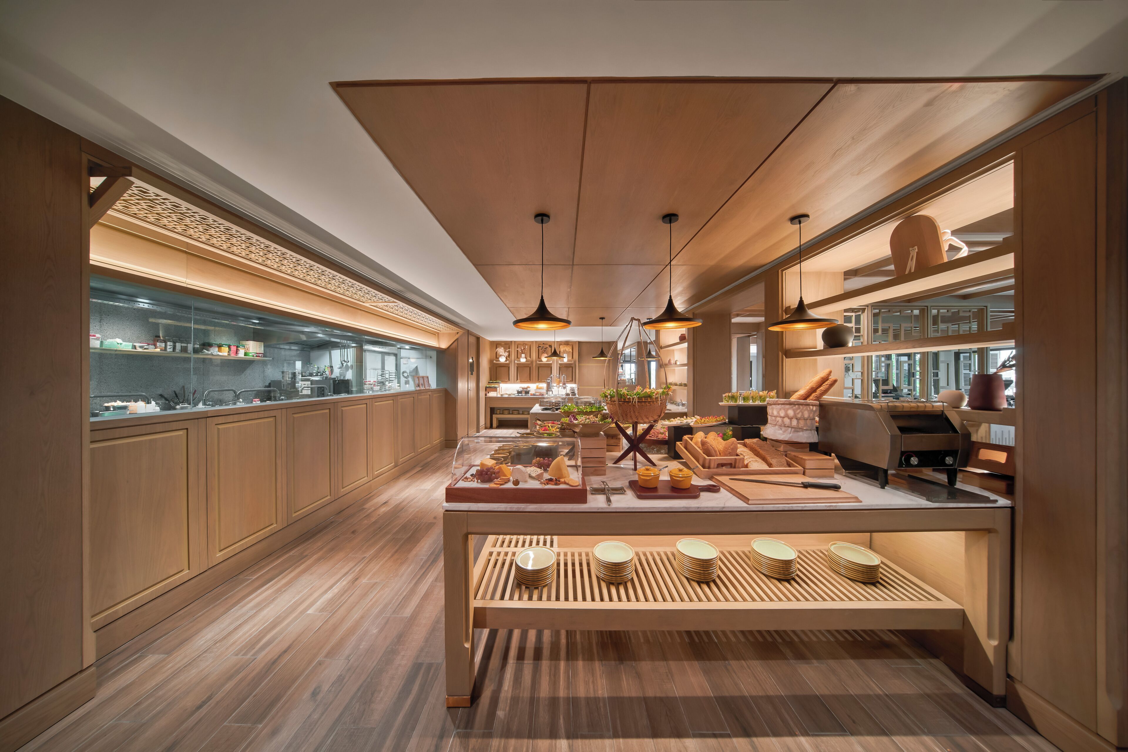 Una cocina moderna con armarios de madera, una isla central con exhibición de alimentos, iluminación colgante y vistas de la ciudad a través de amplias ventanas.