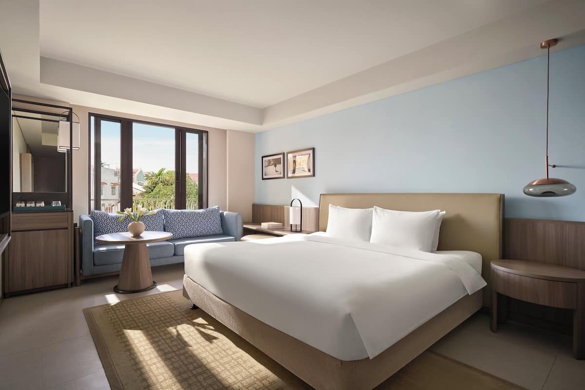 Habitación de hotel moderna con una cama grande, un sofá, una mesita y vistas al exterior.