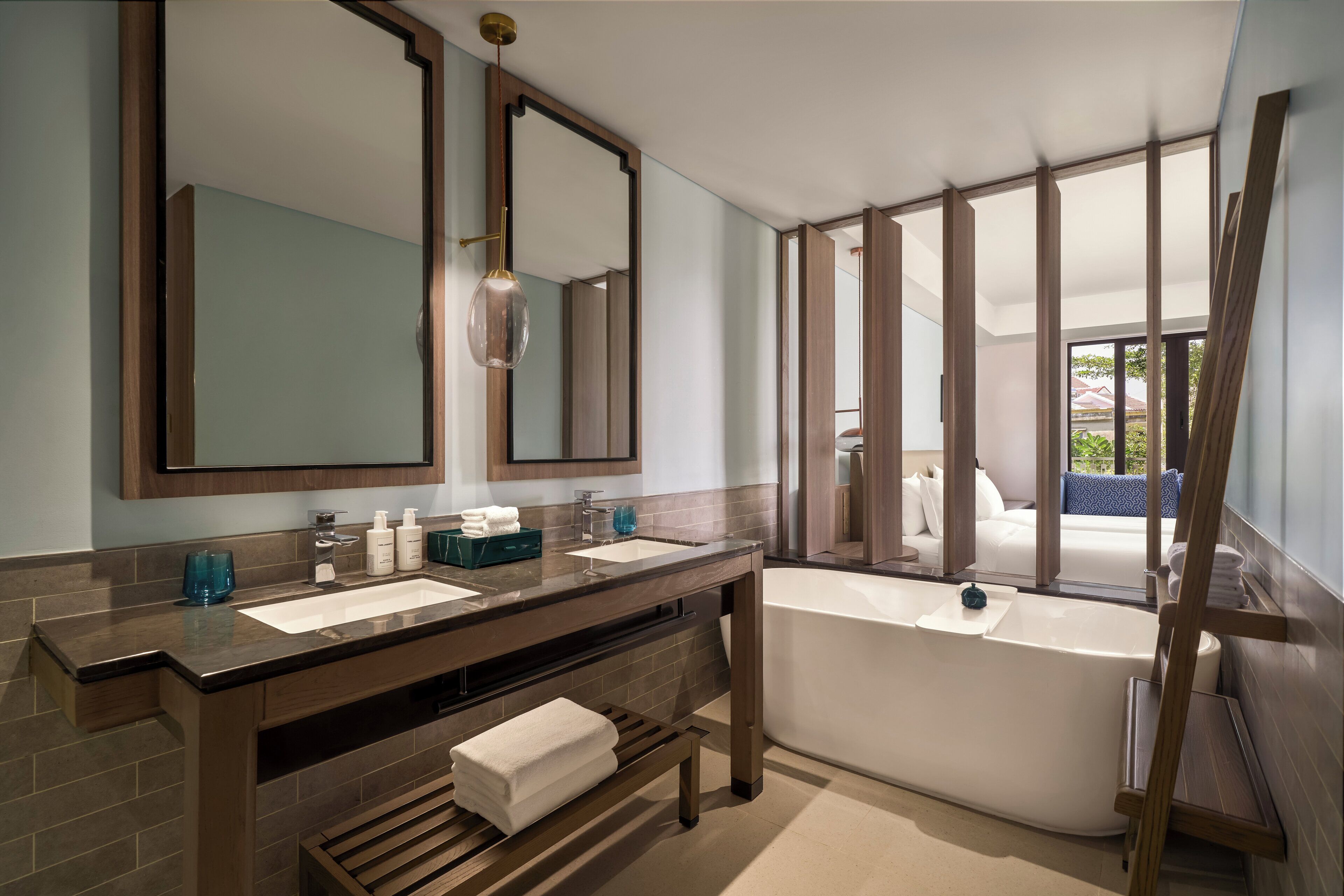 A modern bathroom with a large mirror, two sinks, a bathtub, and a wooden bench.
