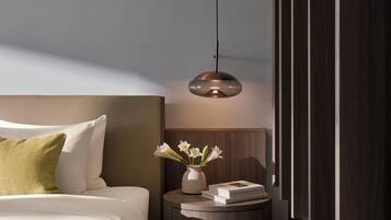 Una habitación de hotel moderna con una cama bien hecha, una mesita de noche con un jarrón de flores y una lámpara colgante.