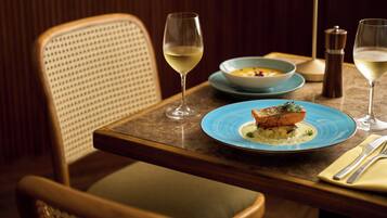 A dining table with a blue plate of food, two wine glasses, a salt and pepper shaker, and a lamp.