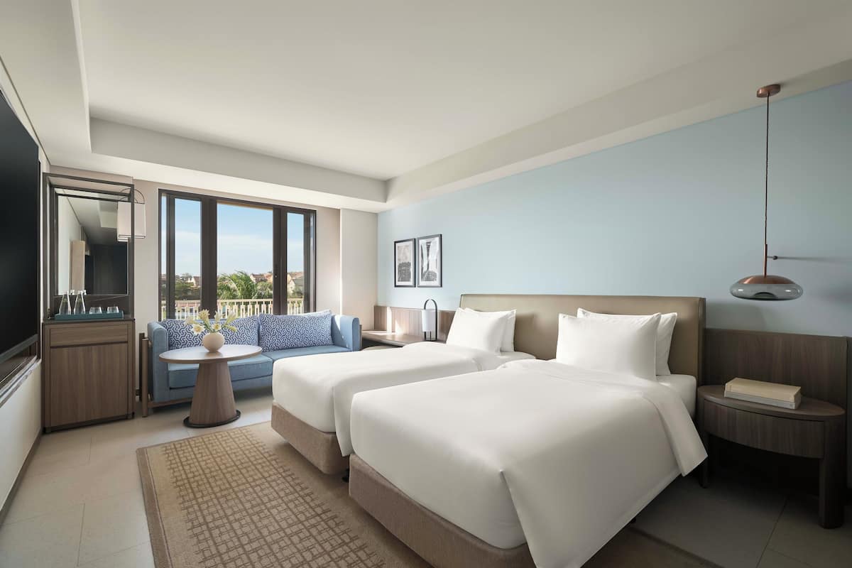 Una habitación de hotel moderna con dos camas, un sofá, un televisor y un balcón con vistas.