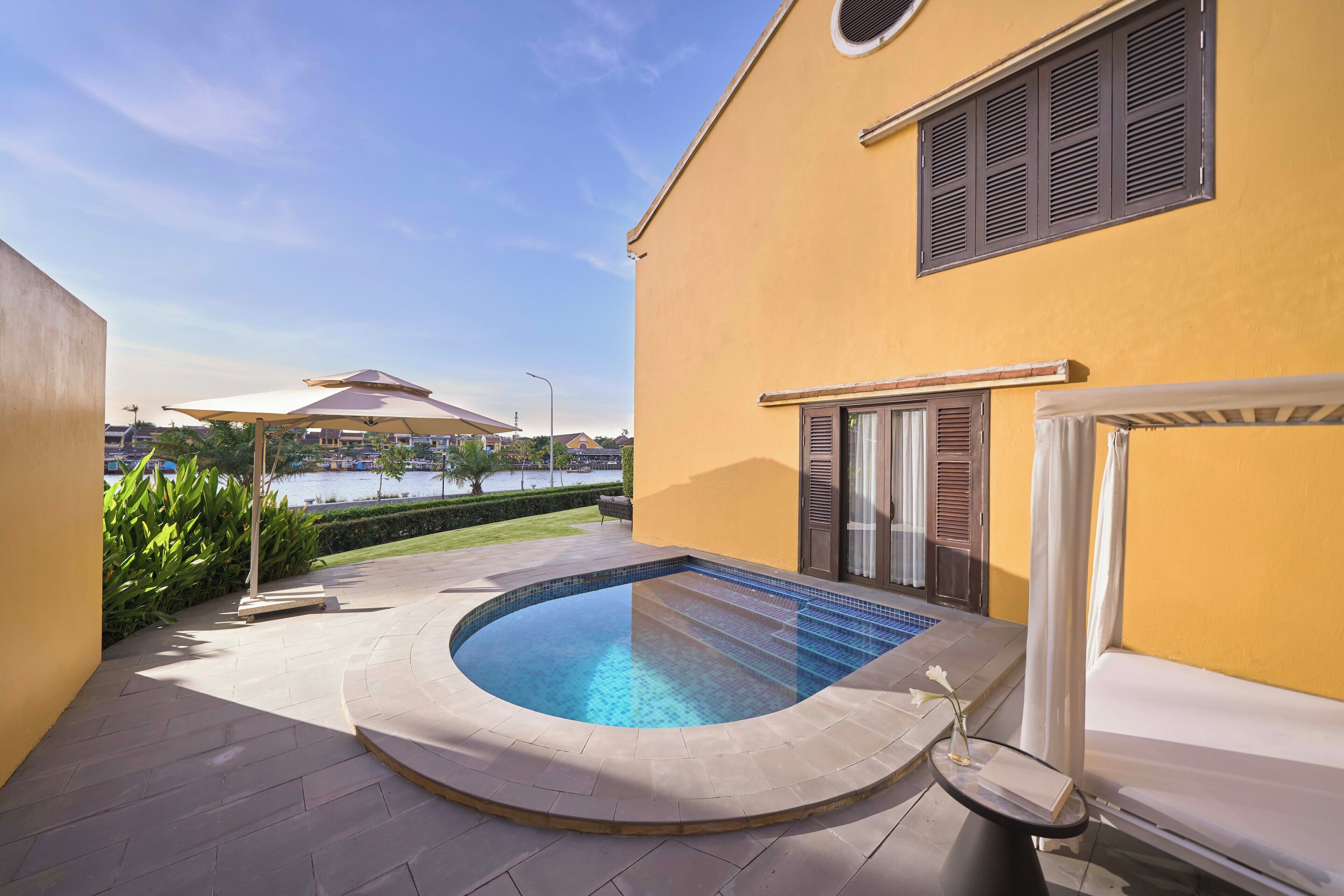 Une piscine avec une terrasse carrelée, un espace salon couvert et une vue sur une étendue d’eau en arrière-plan.