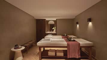 Experience a serene ambiance in this spa room, featuring two massage tables, a wooden bench, and a round side table.