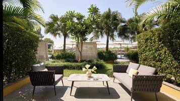 An outdoor seating area with a table and two sofas, surrounded by lush greenery and palm trees.