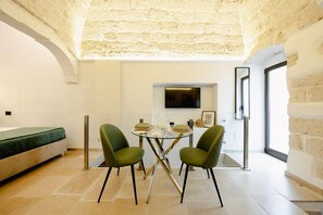 A modern room with a bed, a dining table with chairs, a TV, and a large window.