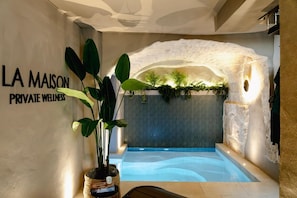Un espace spa avec un panneau mural indiquant « LA MAISON, CENTRE DE BIEN-ĂTRE PRIVà », une grande piscine intĂ©rieure et une plante en pot.