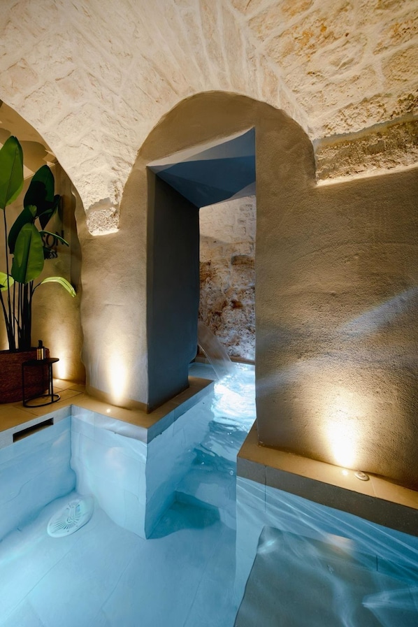 Un espace spa avec des murs en pierre, un Ă©lĂ©ment dĂ©coratif aquatique et un coin salon agrĂ©mentĂ© dâune plante.