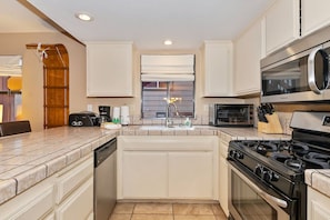 Una cocina con muebles blancos, lavavajillas, estufa, microondas y ventana con vistas.