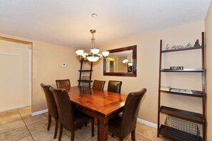 A dining room with a wooden table, six chairs, a chandelier, a mirror, and a bookshelf.