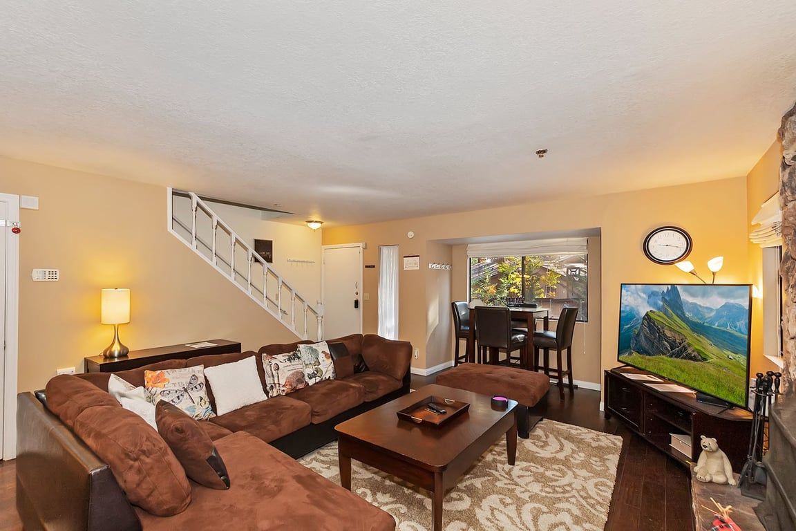 A living room with a brown sofa set, a coffee table, a flat-screen TV, a fireplace, and a staircase leading to another room.