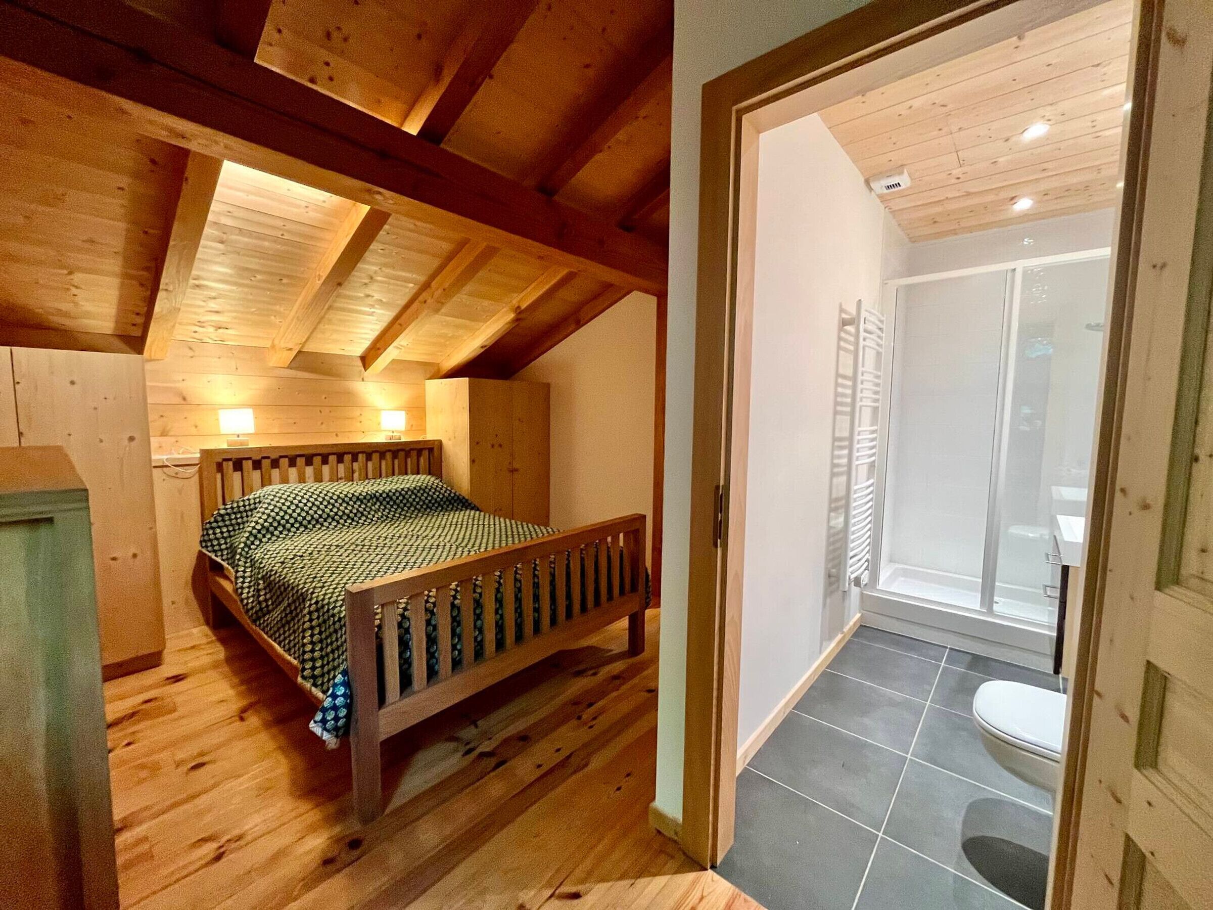 A wooden bedroom with a bed, a wooden ceiling, and a bathroom with a toilet and shower.
