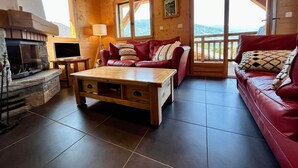Interior acogedor de una cabaña de madera con chimenea, un sofá de cuero rojo, una mesa de centro de madera y un televisor.