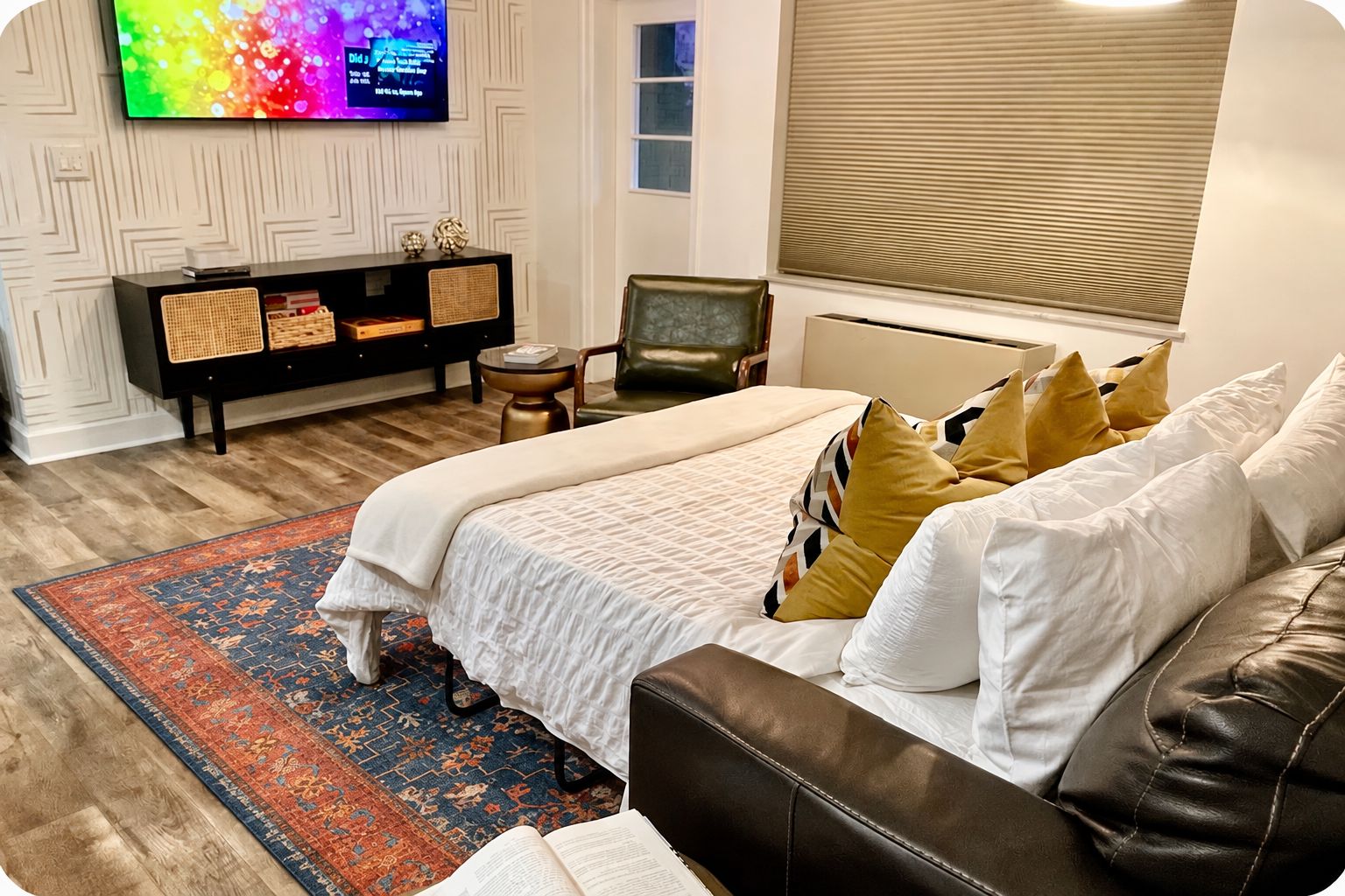 A bedroom with a bed, a sofa, a TV, a small table, and a window with blinds.