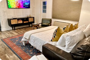 Une chambre à coucher comprenant un lit, un canapé, une télévision, une petite table et une fenêtre avec des stores.
