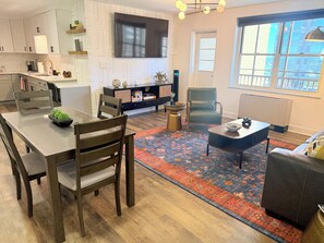 A modern kitchen with white cabinetry, a dining area with a wooden table and chairs, a large window with a view, and a living room with a sofa and a coffee table. - Downtown High-Rise, 19th floor with City Views (Atlanta)