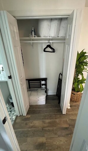 Un couloir étroit avec un banc en bois, un portant à vêtements suspendu et une plante en pot.