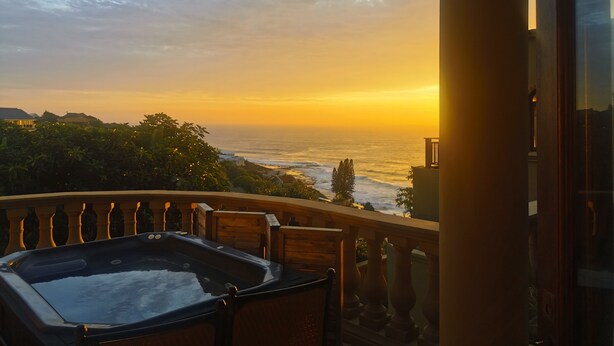 A balcony with a hot tub, overlooking a coastal view during sunset.