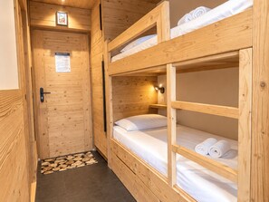 Quarto com beliche de madeira, porta e uma pequena prateleira.