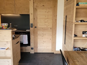 Cozinha compacta com armários de madeira, forno embutido e bancada pequena com chaleira e garrafa.