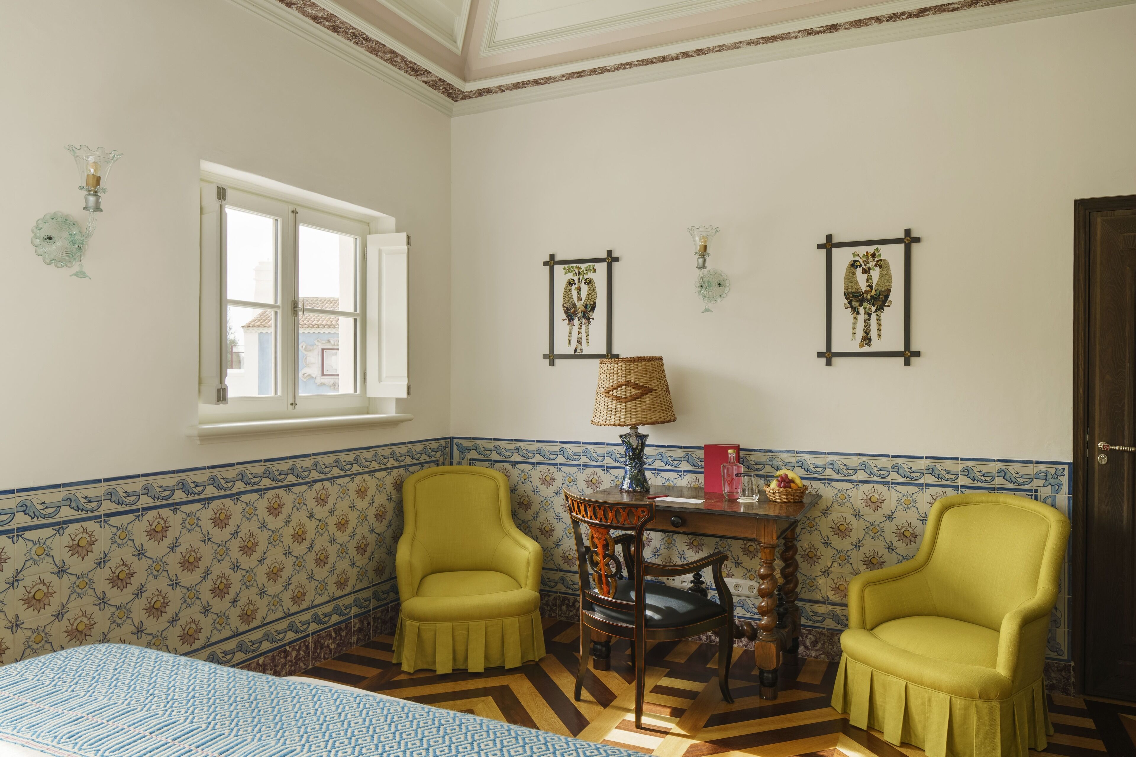 Una habitación con dos sillones amarillos, una mesa de madera con una lámpara y una ventana que ofrece vistas a edificios.