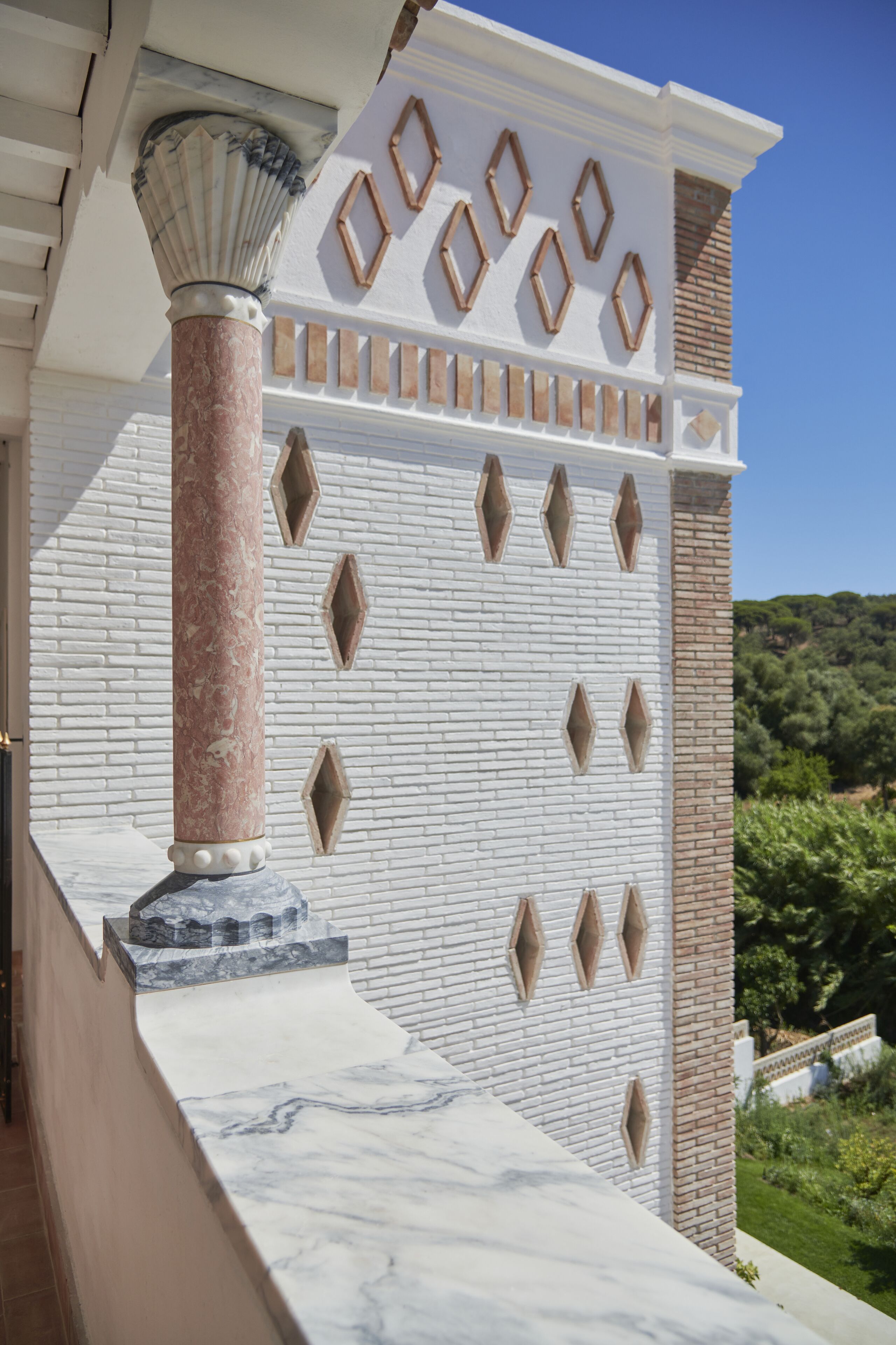 Un muro de ladrillo blanco con aberturas en forma de diamante y una columna de mármol.