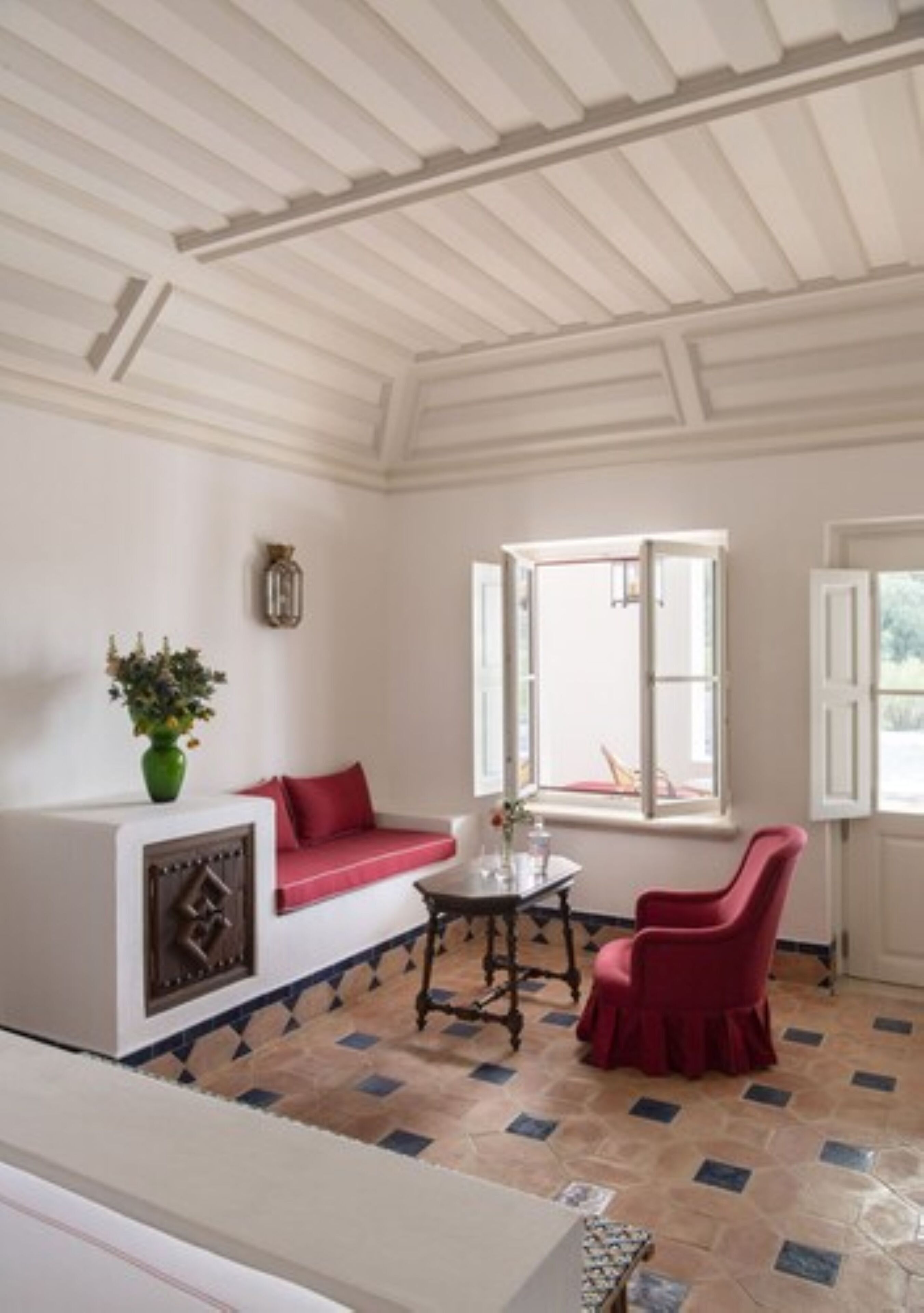 A room with a white ceiling, a red sofa, a table with a vase, and a chair.