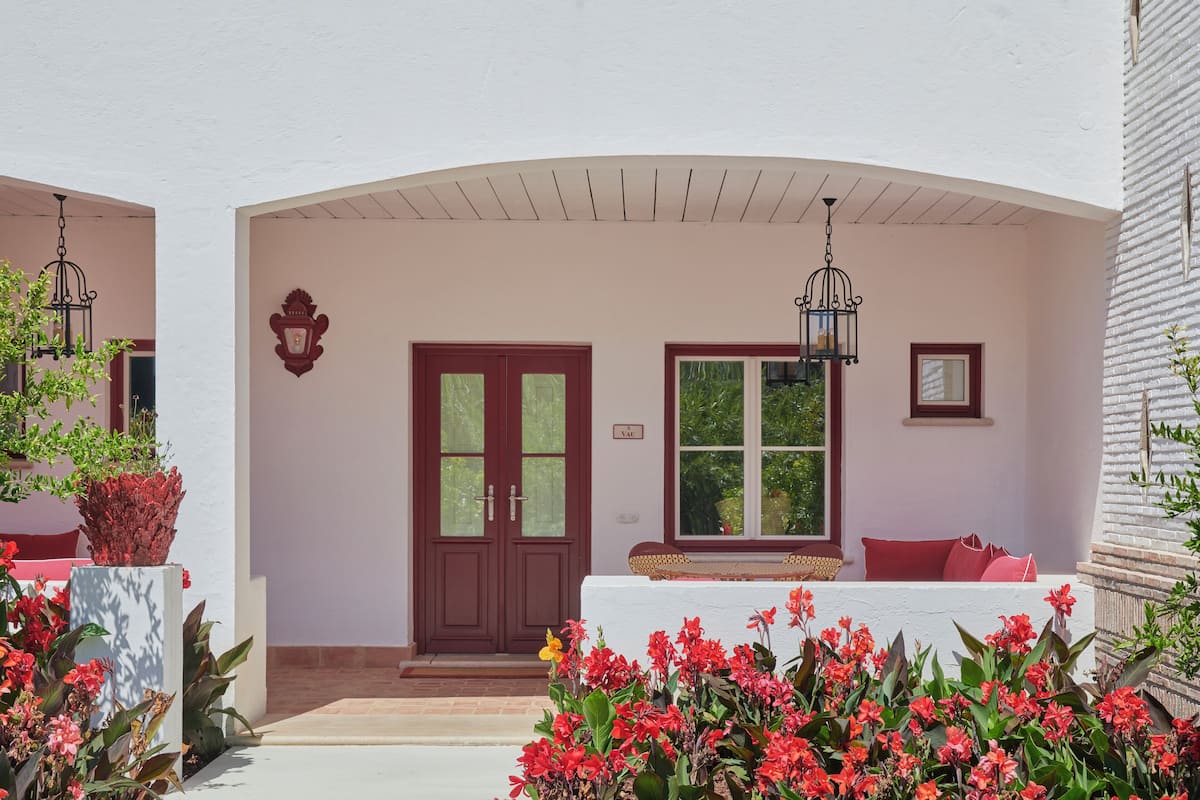 A covered entrance with a red door, a bench with red cushions, and a wall-mounted sign.