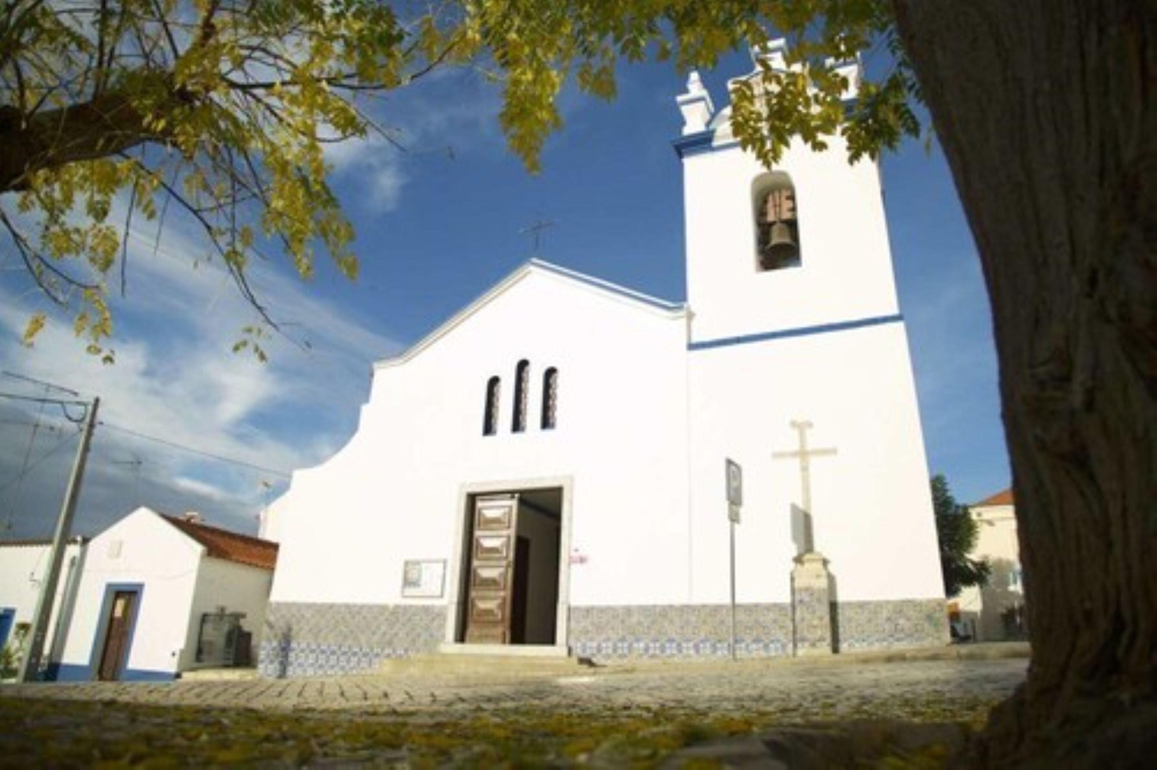 Igreja branca com uma torre de sino e uma cruz em frente.