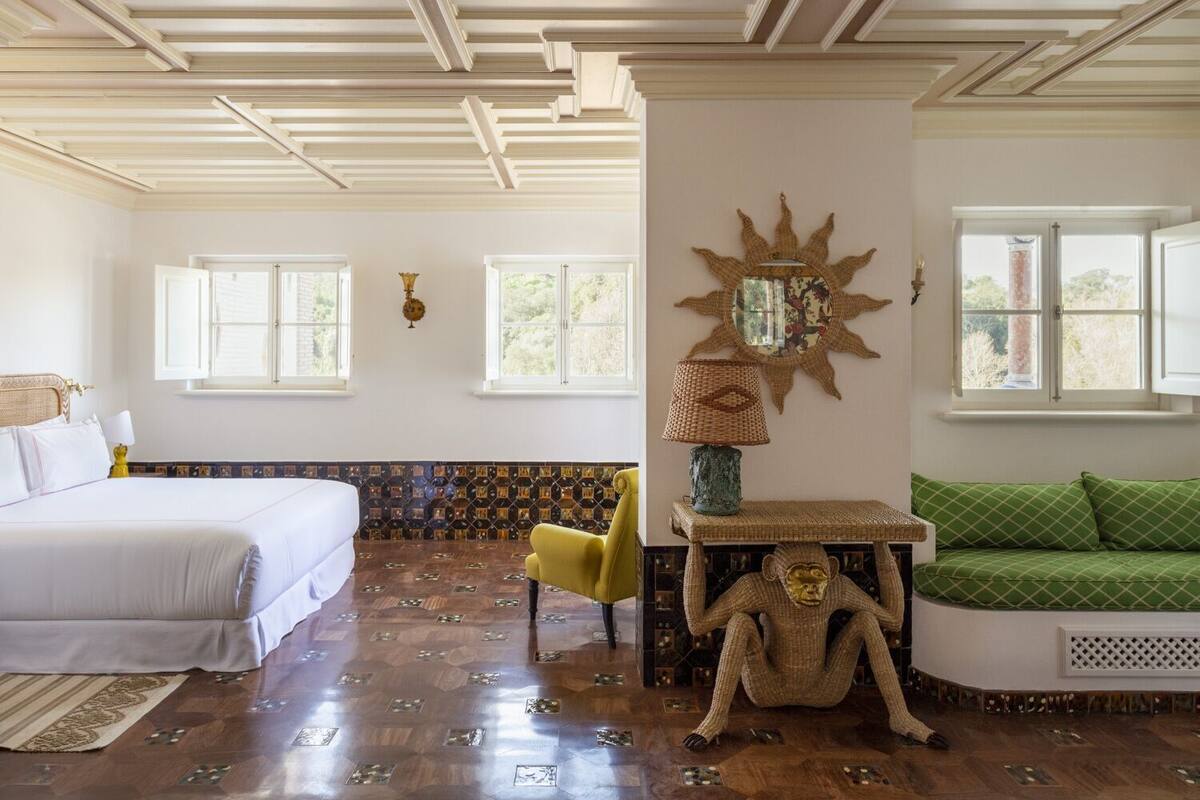 A room with a bed, a sofa, a chair, a decorative wall piece, and a window.