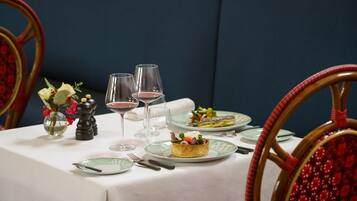 Una mesa de comedor dispuesta con platos, cubiertos, un florero con flores y dos copas de vino tinto.