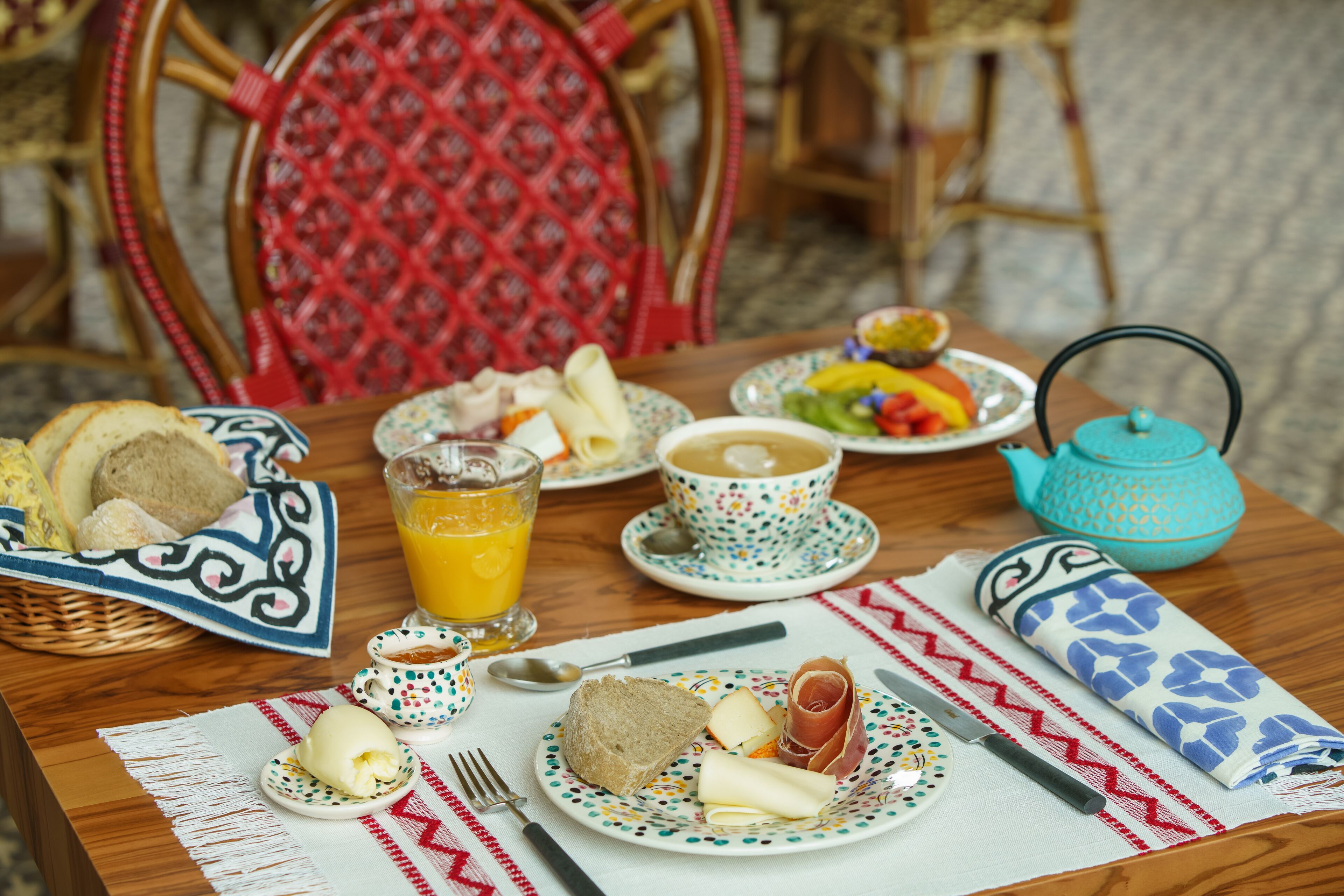 A breakfast table with plates of food, a teapot, and a glass of orange juice.