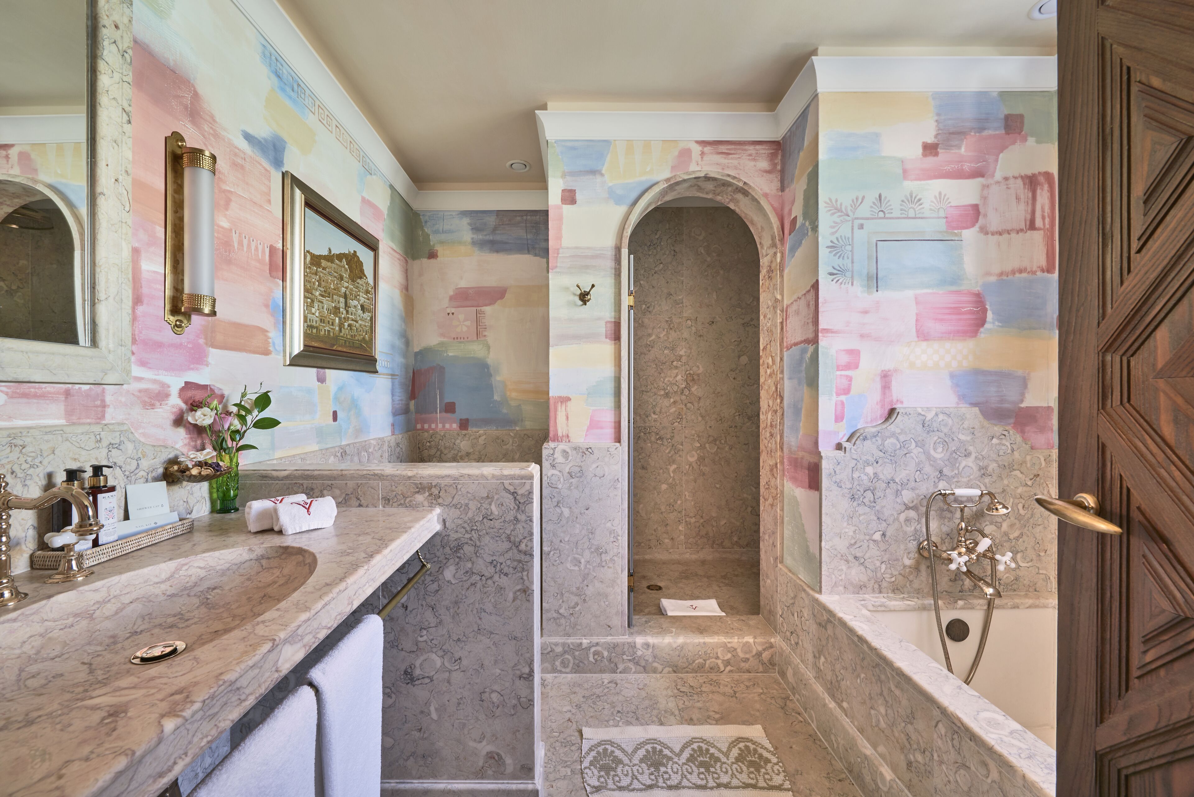 A bathroom with a marble sink, a bathtub with a showerhead, and a wall with a colorful abstract design.