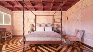 A four-poster bed with a patterned bedspread, a wooden floor with a geometric design, and a pink and white color scheme.